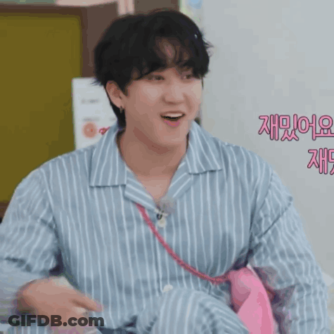 A Man Wearing A Blue And White Striped Shirt Is Smiling And Holding A Pink Tie GIF