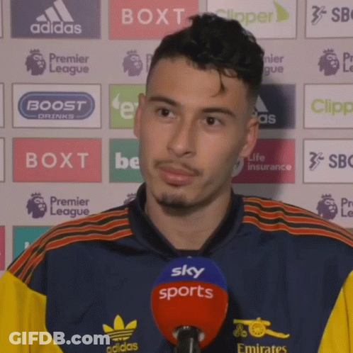 A Man Wearing A Blue And Yellow Adidas Shirt Is Talking Into A Microphone GIF