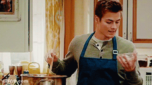 A Man Wearing A Blue Apron Is Cooking In A Kitchen . GIF
