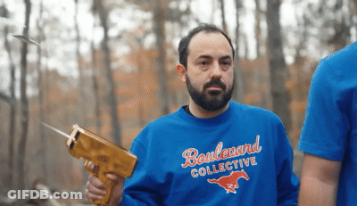 A Man Wearing A Blue Boulevard Collective Sweatshirt Is Holding A Gun GIF