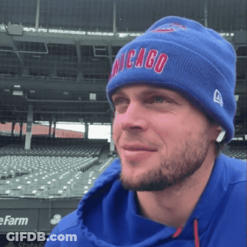 A Man Wearing A Blue Chicago Beanie Stands In Front Of An Empty Stadium GIF