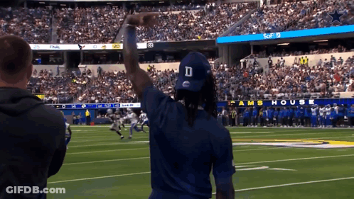 A Man Wearing A Blue D Hat Stands On A Football Field GIF