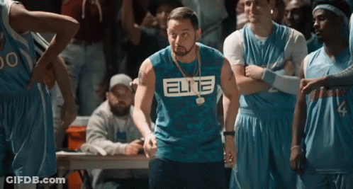 A Man Wearing A Blue Elite Shirt Is Standing In Front Of A Basketball Team . GIF