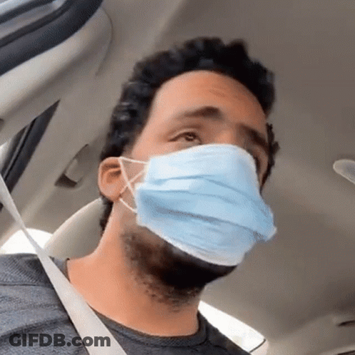 A Man Wearing A Blue Face Mask Is Sitting In A Car With A Seat Belt . GIF