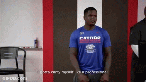 A Man Wearing A Blue Gators Shirt Is Standing In A Room . GIF