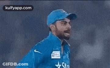 A Man Wearing A Blue Hat And A Blue Jacket With A Star On It Is Walking On A Field . GIF