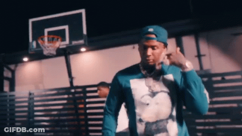 A Man Wearing A Blue Hat And A Blue Shirt Is Standing In Front Of A Basketball Court . GIF