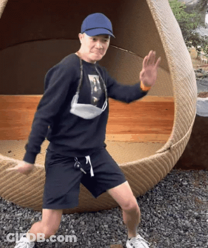 A Man Wearing A Blue Hat And A Face Mask Is Standing In Front Of A Wicker Chair GIF