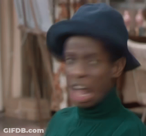 A Man Wearing A Blue Hat And A Green Turtleneck Sweater Is Making A Funny Face . GIF