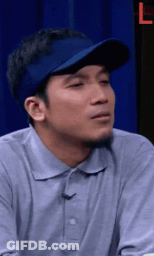 A Man Wearing A Blue Hat And A Grey Shirt Is Making A Face . GIF