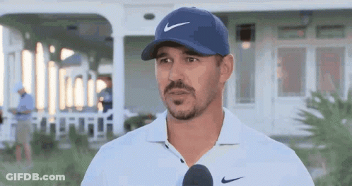 A Man Wearing A Blue Hat And A White Shirt Is Talking Into A Microphone . GIF