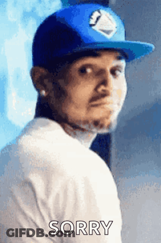 A Man Wearing A Blue Hat And A White Shirt With The Word Sorry On It GIF
