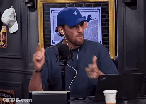 A Man Wearing A Blue Hat And Ear Buds Talking Into A Microphone GIF
