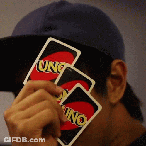 A Man Wearing A Blue Hat Holds Two Uno Cards In Front Of His Face GIF