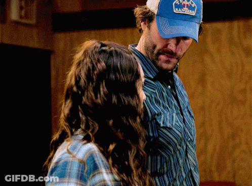 A Man Wearing A Blue Hat That Says Rancho Stands Next To A Woman GIF
