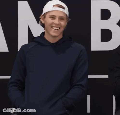 A Man Wearing A Blue Hoodie And A White Hat Is Smiling With A Question Mark In Front Of Him GIF