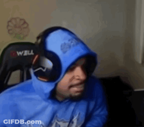 A Man Wearing A Blue Hoodie And Headphones Is Sitting In A Chair In Front Of A Computer . GIF