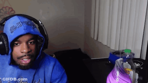 A Man Wearing A Blue Hoodie And Headphones Is Sitting In Front Of A Computer . GIF