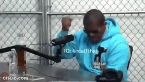 A Man Wearing A Blue Hoodie Is Sitting In Front Of A Microphone . GIF