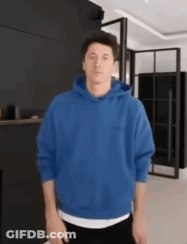 A Man Wearing A Blue Hoodie Is Standing In A Living Room . GIF