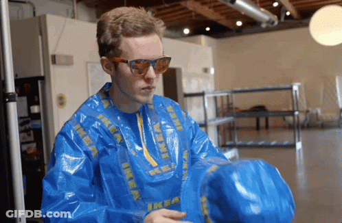 A Man Wearing A Blue Ikea Jacket And Sunglasses Holds A Blue Bag GIF