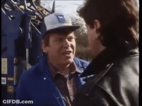 A Man Wearing A Blue Jacket And A White Hat With The Letter M On It Talks To Another Man GIF