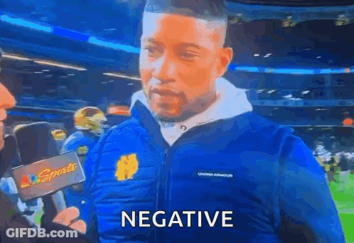 A Man Wearing A Blue Jacket Is Talking Into A Microphone And The Word Negative Is On The Screen . GIF