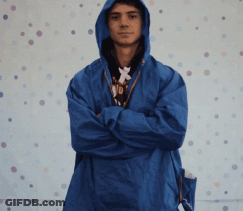 A Man Wearing A Blue Jacket With A Hood Has His Arms Crossed In Front Of A Polka Dot Background GIF