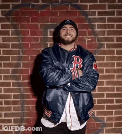 A Man Wearing A Blue Jacket With The Letter B On It Stands In Front Of A Brick Wall GIF