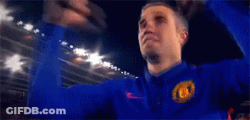 A Man Wearing A Blue Jacket With The Manchester United Logo On It Is Raising His Fist In The Air . GIF