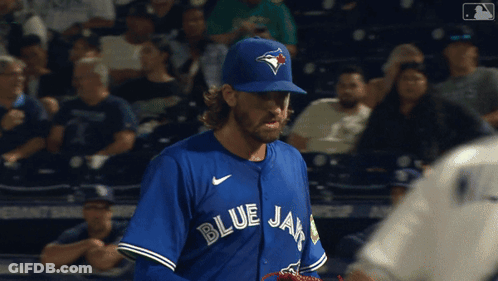 A Man Wearing A Blue Jays Jersey Stands In A Crowd GIF