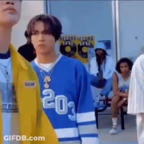 A Man Wearing A Blue Jersey And A Yellow Jacket Is Standing In A Crowd Of People . GIF