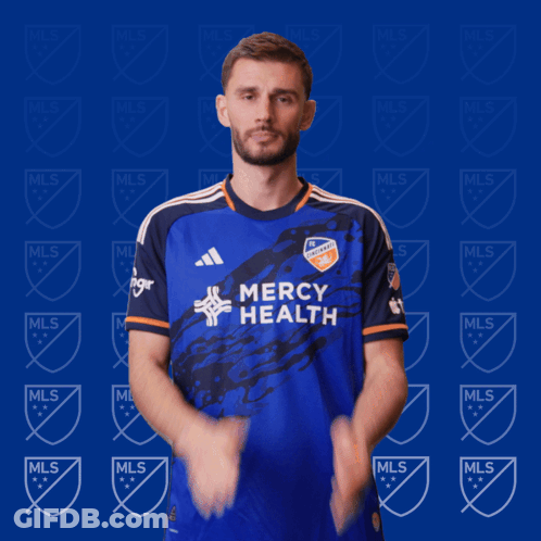 A Man Wearing A Blue Mercy Health Jersey Is Clapping His Hands GIF