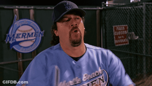 A Man Wearing A Blue Mermen Baseball Jersey Stands In Front Of A Fence GIF