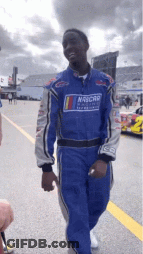 A Man Wearing A Blue Nascar Suit Walks Down A Road GIF