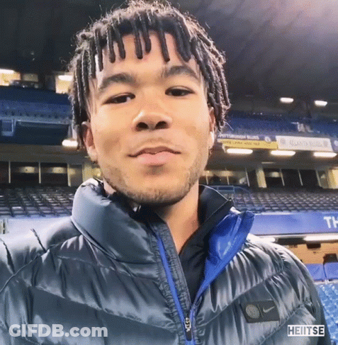 A Man Wearing A Blue Nike Jacket Stands In Front Of A Stadium GIF