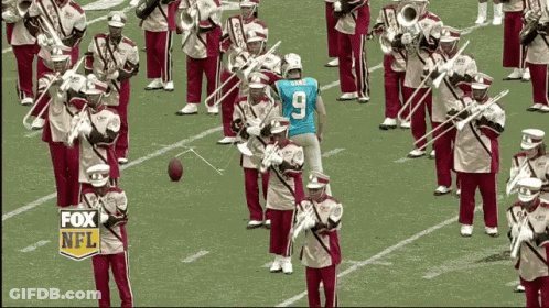 A Man Wearing A Blue Number 9 Jersey Stands In Front Of A Marching Band GIF