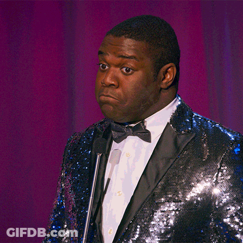 A Man Wearing A Blue Sequined Jacket And Bow Tie Stands In Front Of A Microphone GIF
