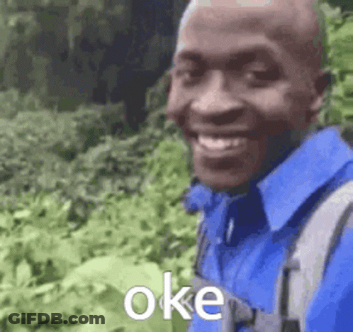 A Man Wearing A Blue Shirt And A Backpack Is Smiling And Standing In A Field . GIF