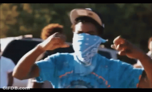 A Man Wearing A Blue Shirt And A Bandana On His Face Is Making A Fist . GIF