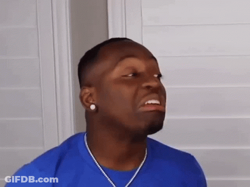 A Man Wearing A Blue Shirt And A Necklace Is Making A Face . GIF