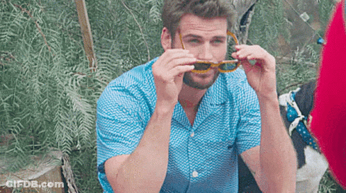A Man Wearing A Blue Shirt And Sunglasses Is Sitting On A Chair . GIF