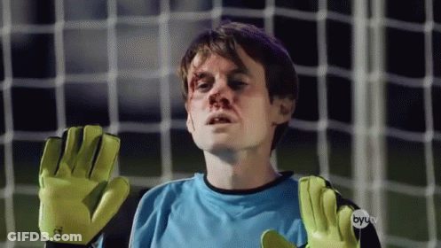 A Man Wearing A Blue Shirt And Yellow Gloves Stands In Front Of A Soccer Net GIF