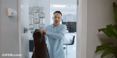 A Man Wearing A Blue Shirt Is Holding A Black Jacket GIF
