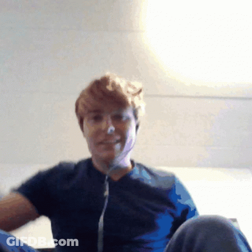A Man Wearing A Blue Shirt Is Sitting On A Bed GIF