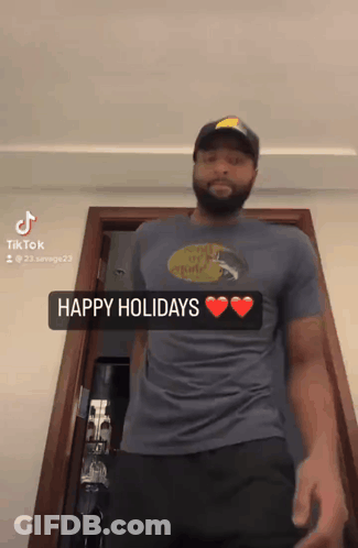 A Man Wearing A Blue Shirt That Says Happy Holidays Is Standing In Front Of A Door GIF