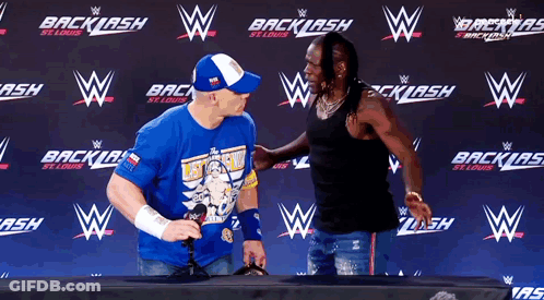 A Man Wearing A Blue Shirt That Says " Let 'S Go " Stands Next To Another Man GIF