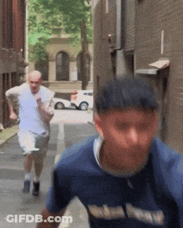 A Man Wearing A Blue Shirt That Says ' Washington ' On It Is Running Down A Street GIF