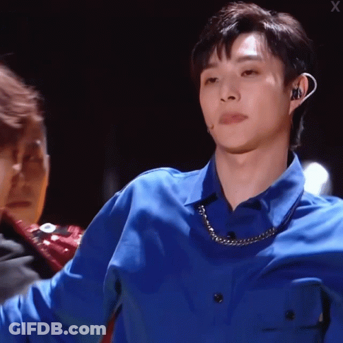 A Man Wearing A Blue Shirt With A Chain Around His Neck Looks At The Camera GIF