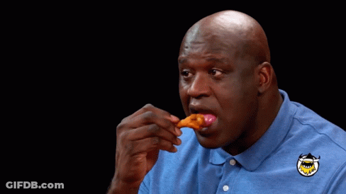 A Man Wearing A Blue Shirt With A Shark On It Is Eating A Piece Of Food GIF